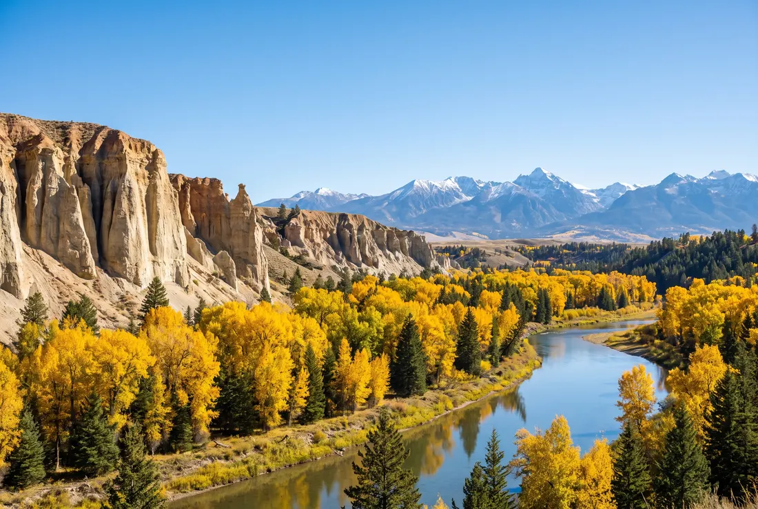 Pale hoodoo cliffs above a river valley with golden cottonwoods, mountains behind. Generated image of the landscape type, not a specific place.